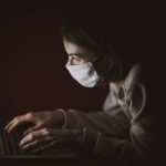 lady in front of laptop wearing mask in a dark room